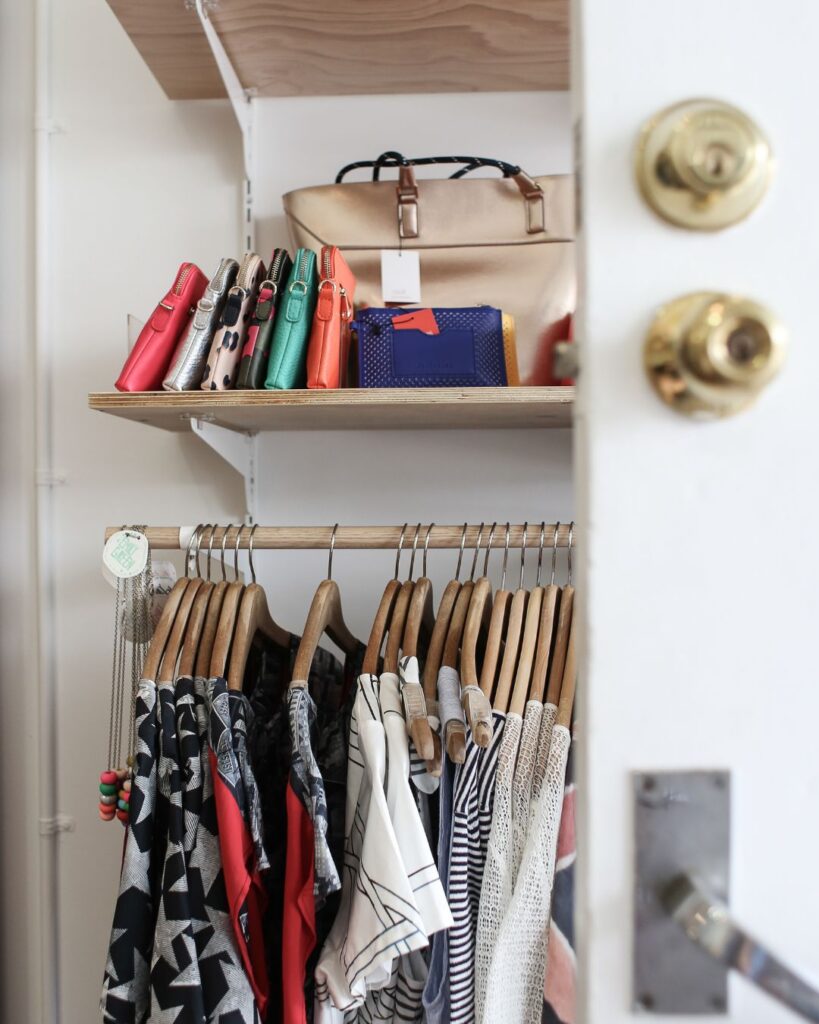 declutter photo of a closet with several hanging shirts and a shelf with some purses 
